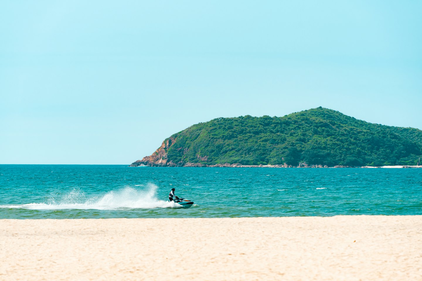 A person rides a jet ski across the tropical ocean.
