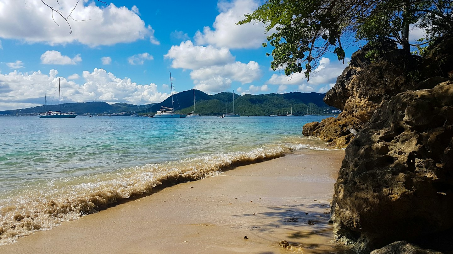 Sailboats anchor in turquoise water off a tropical beach.