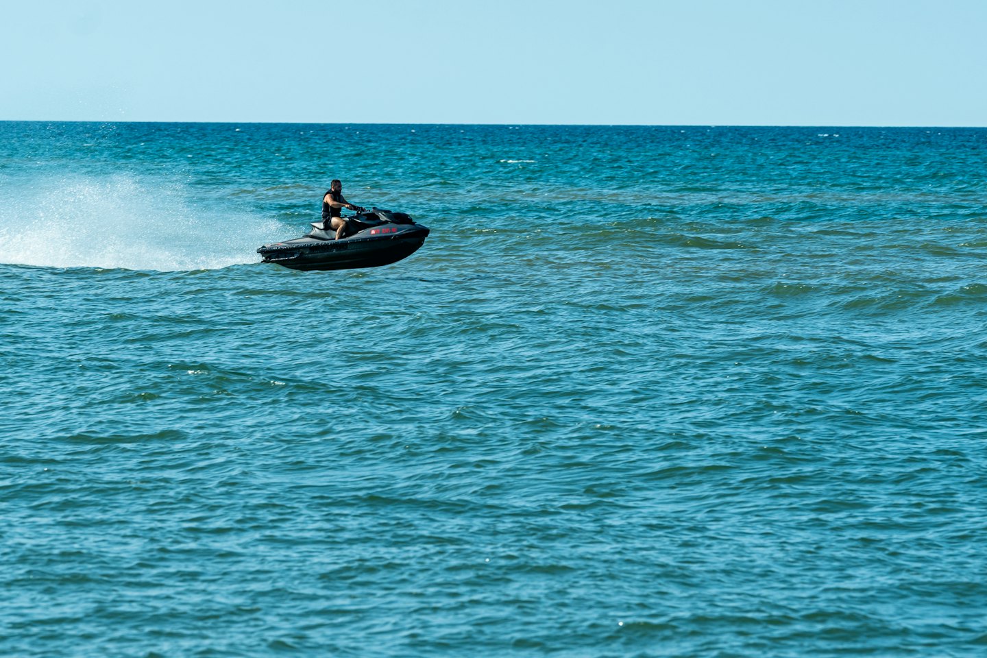A man rides a black jet ski across choppy blue ocean.